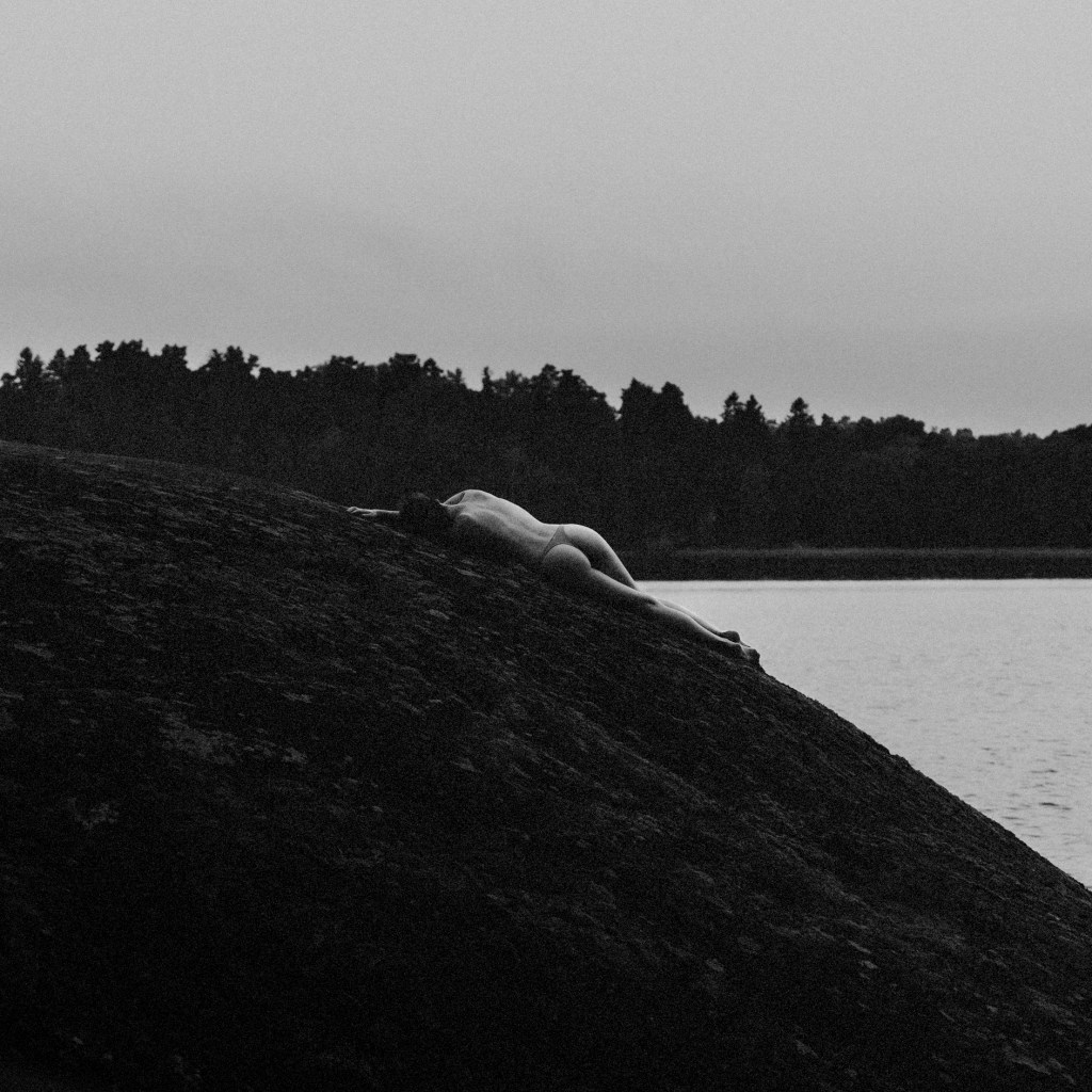 portrait of a woman laying bare-skinned on rock in a melancholic state