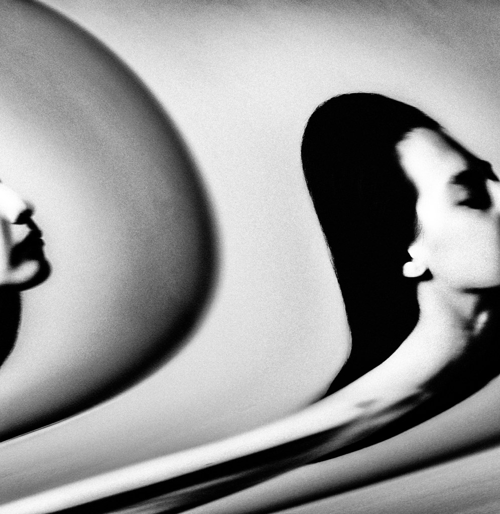 Abstract black and white image of a woman's face, distorted with fluid motion. The scene conveys mystery and introspection against a blurred background.